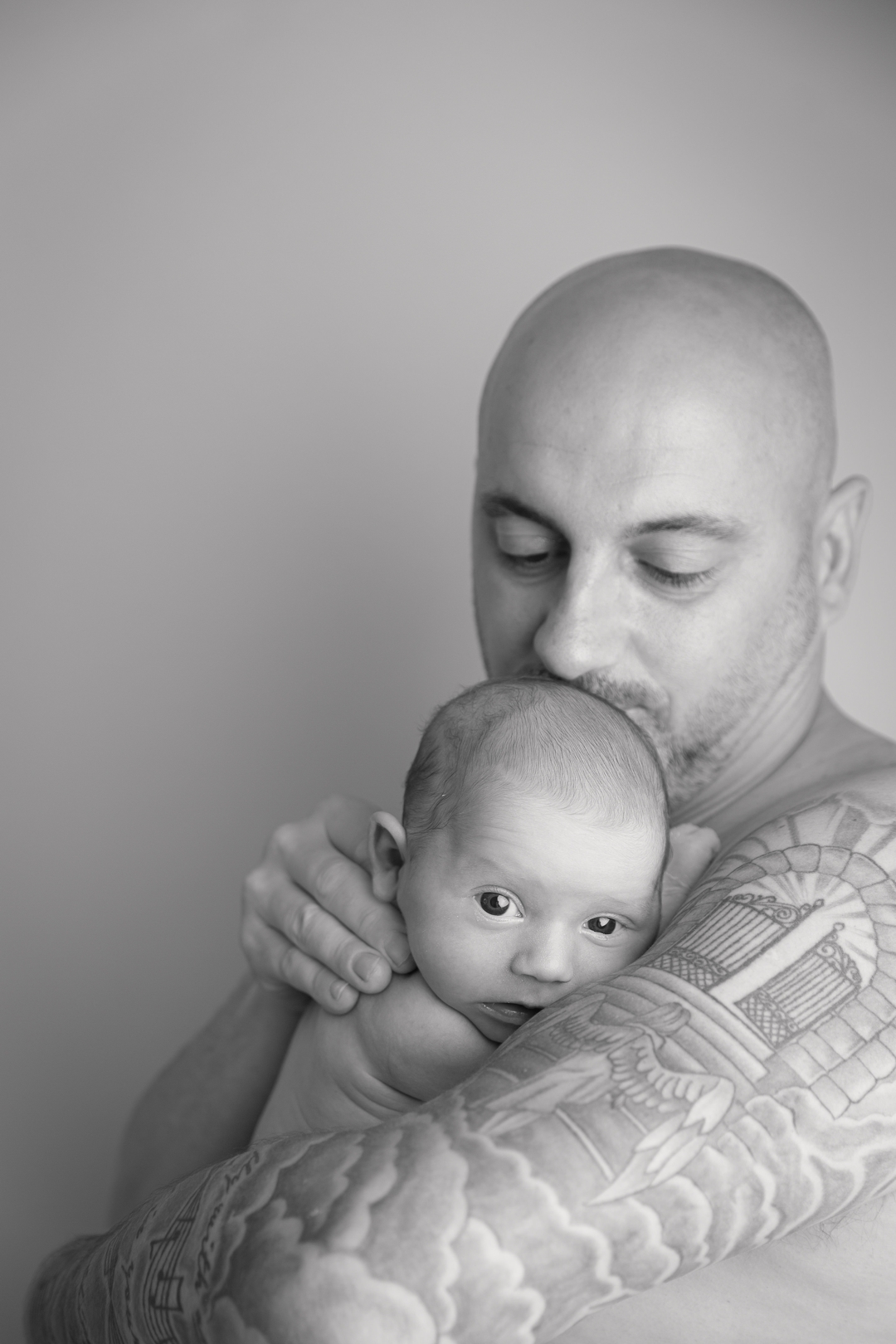 Newborn photography by hayley morris photography - newborn photographer in malvern worcestershire - image shows a new dad with tattoos doing a skin to skin photo holding his newborn baby